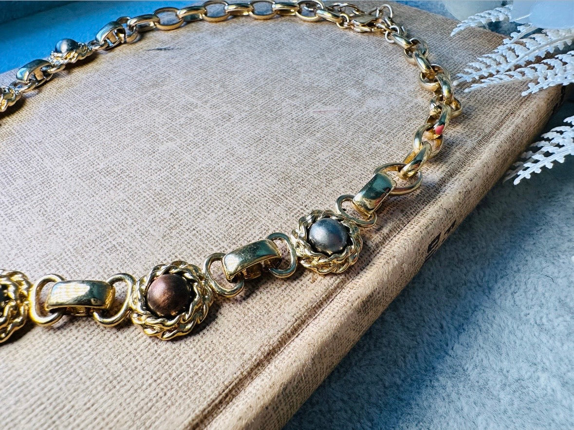 This vintage Etruscan style Liz Claiborne gold chain necklace is a beautifully unique find. Featuring large curb chain links with round cabochons of faux hematite and bronze set in gold bezels. In the center is a larger bronzed oval cabochon in the same style of gold roped bezel. Signed on back of center cabochon as well as the signature LCI triangle hang tag on the end of extender chain. Versatile while making a statement, and incredibly flattering. Minimal wear from age, no major flaws to note; &nbsp;in g