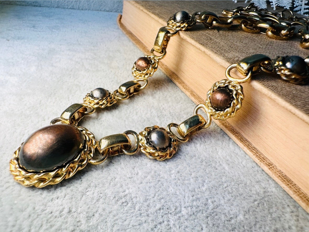 This vintage Etruscan style Liz Claiborne gold chain necklace is a beautifully unique find. Featuring large curb chain links with round cabochons of faux hematite and bronze set in gold bezels. In the center is a larger bronzed oval cabochon in the same style of gold roped bezel. Signed on back of center cabochon as well as the signature LCI triangle hang tag on the end of extender chain. Versatile while making a statement, and incredibly flattering. Minimal wear from age, no major flaws to note; &nbsp;in g