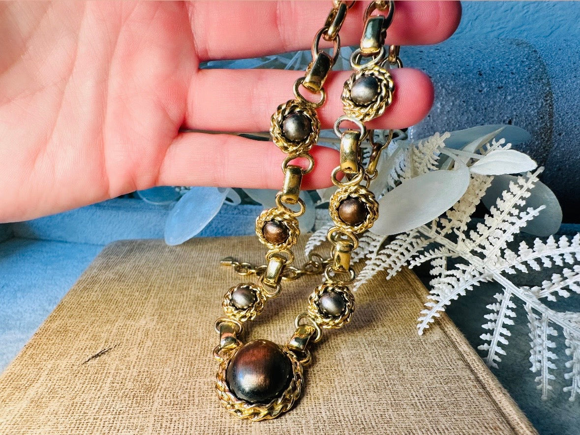 This vintage Etruscan style Liz Claiborne gold chain necklace is a beautifully unique find. Featuring large curb chain links with round cabochons of faux hematite and bronze set in gold bezels. In the center is a larger bronzed oval cabochon in the same style of gold roped bezel. Signed on back of center cabochon as well as the signature LCI triangle hang tag on the end of extender chain. Versatile while making a statement, and incredibly flattering. Minimal wear from age, no major flaws to note; &nbsp;in g