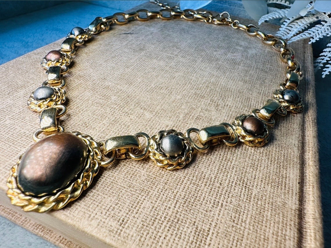 This vintage Etruscan style Liz Claiborne gold chain necklace is a beautifully unique find. Featuring large curb chain links with round cabochons of faux hematite and bronze set in gold bezels. In the center is a larger bronzed oval cabochon in the same style of gold roped bezel. Signed on back of center cabochon as well as the signature LCI triangle hang tag on the end of extender chain. Versatile while making a statement, and incredibly flattering. Minimal wear from age, no major flaws to note; &nbsp;in g