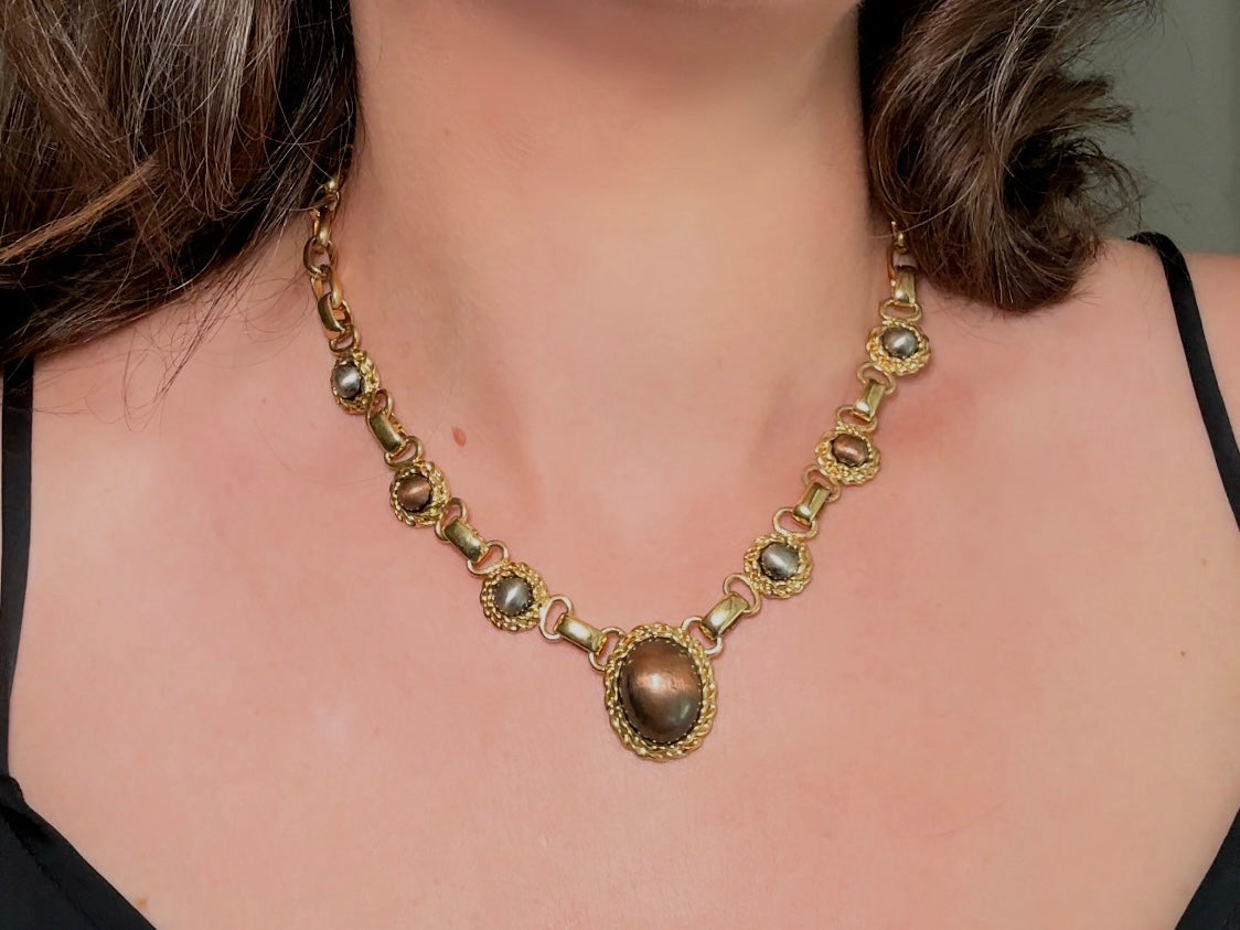 This vintage Etruscan style Liz Claiborne gold chain necklace is a beautifully unique find. Featuring large curb chain links with round cabochons of faux hematite and bronze set in gold bezels. In the center is a larger bronzed oval cabochon in the same style of gold roped bezel. Signed on back of center cabochon as well as the signature LCI triangle hang tag on the end of extender chain. Versatile while making a statement, and incredibly flattering. Minimal wear from age, no major flaws to note; &nbsp;in g