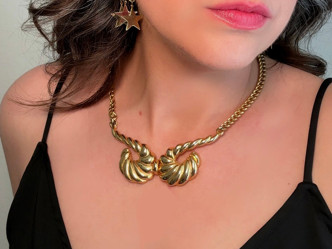 This 1970s vintage gold necklace is such a striking and unique piece. Featuring gold curb chain and a striking centerpiece of two textured gold horns. Full of vintage flair, this centerpiece is dimensional and stunning. This choker necklace is so flattering on and the perfect collar length. 