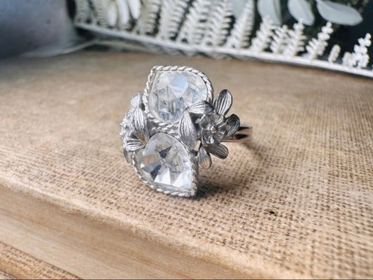 This beautiful sparkling vintage ring features two diamond heart rhinestones flanked by a flower and leaves on each side. &nbsp;Made in the 70's this sparkly ring is a wonderfully thoughtful vintage gift for an April birthday. Great vintage condition, very minor wear, no flaws to note- please see pics.

Dimensions: size 9 max and adjustable to be smaller