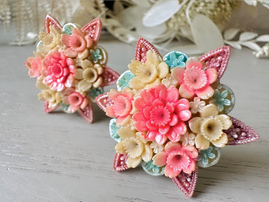 These vintage 1950s Japanese floral celluloid earrings are so colorful. Carved celluloid bursting with sakura blossoms and flowers, these earrings are on the larger side and are painted with a beautiful pearlized pink, blue and light cream. The star-shaped base and raised beaded edges are also characteristic of vintage Japanese celluloid jewelry. They are 1.5" in size.