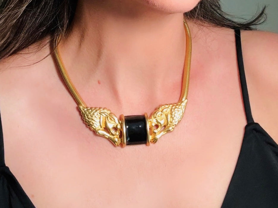 This bold vintage Etruscan style double lion necklace is truly incredible. Featuring two intricate sculptural gold lions on either side of a black enamel focal. This vintage collar necklace is the height of 80s glam, with its contrasting shiny black enamel and matte satin gold components. Wide snake chain and an oversized clasp complete this sensational necklace. 