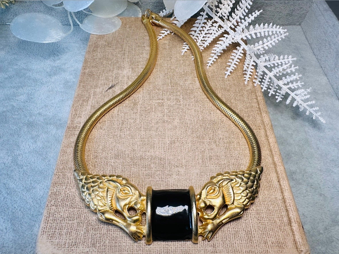 This bold vintage Etruscan style double lion necklace is truly incredible. Featuring two intricate sculptural gold lions on either side of a black enamel focal. This vintage collar necklace is the height of 80s glam, with its contrasting shiny black enamel and matte satin gold components. Wide snake chain and an oversized clasp complete this sensational necklace. 