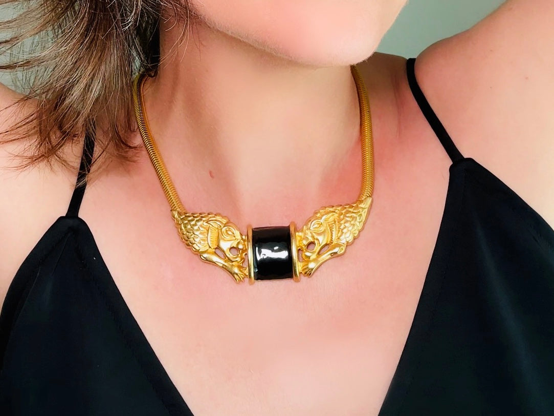 This bold vintage Etruscan style double lion necklace is truly incredible. Featuring two intricate sculptural gold lions on either side of a black enamel focal. This vintage collar necklace is the height of 80s glam, with its contrasting shiny black enamel and matte satin gold components. Wide snake chain and an oversized clasp complete this sensational necklace. 