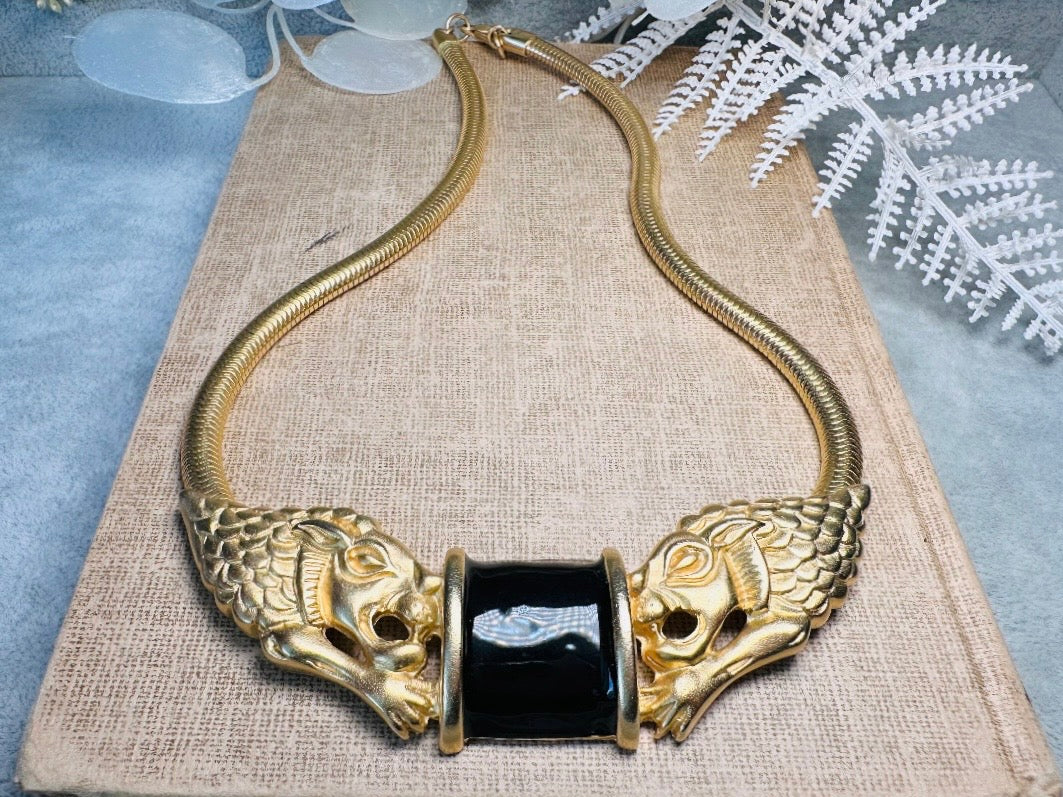 This bold vintage Etruscan style double lion necklace is truly incredible. Featuring two intricate sculptural gold lions on either side of a black enamel focal. This vintage collar necklace is the height of 80s glam, with its contrasting shiny black enamel and matte satin gold components. Wide snake chain and an oversized clasp complete this sensational necklace. 