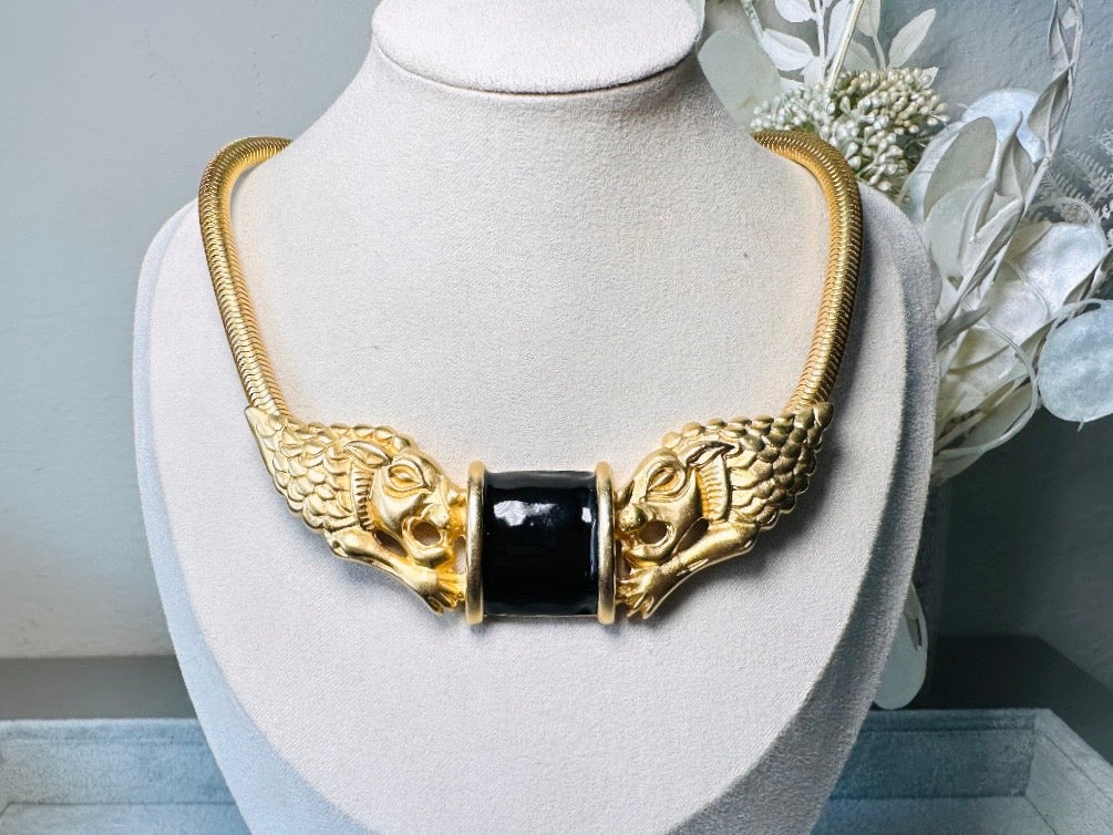 This bold vintage Etruscan style double lion necklace is truly incredible. Featuring two intricate sculptural gold lions on either side of a black enamel focal. This vintage collar necklace is the height of 80s glam, with its contrasting shiny black enamel and matte satin gold components. Wide snake chain and an oversized clasp complete this sensational necklace. 