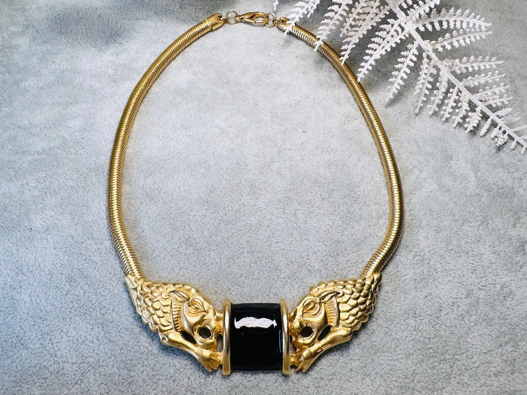 This bold vintage Etruscan style double lion necklace is truly incredible. Featuring two intricate sculptural gold lions on either side of a black enamel focal. This vintage collar necklace is the height of 80s glam, with its contrasting shiny black enamel and matte satin gold components. Wide snake chain and an oversized clasp complete this sensational necklace. 