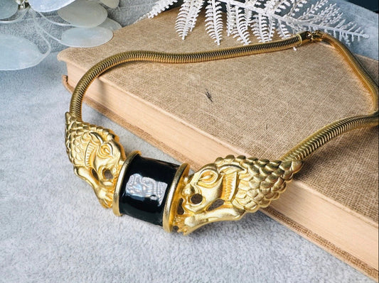 This bold vintage Etruscan style double lion necklace is truly incredible. Featuring two intricate sculptural gold lions on either side of a black enamel focal. This vintage collar necklace is the height of 80s glam, with its contrasting shiny black enamel and matte satin gold components. Wide snake chain and an oversized clasp complete this sensational necklace. 