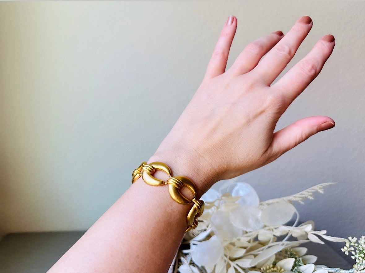 This is a matte gold chain link vintage bracelet by Premier Designs. The links are round and wide with textured ribbing in the center. The finish is a satin matte gold. Very popular style in the 1980s and modern. Shown worn on wrist.