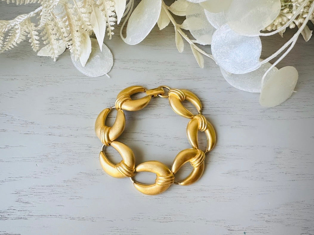 This is a matte gold chain link vintage bracelet by Premier Designs. The links are round and wide with textured ribbing in the center. The finish is a satin matte gold. Very popular style in the 1980s and modern.