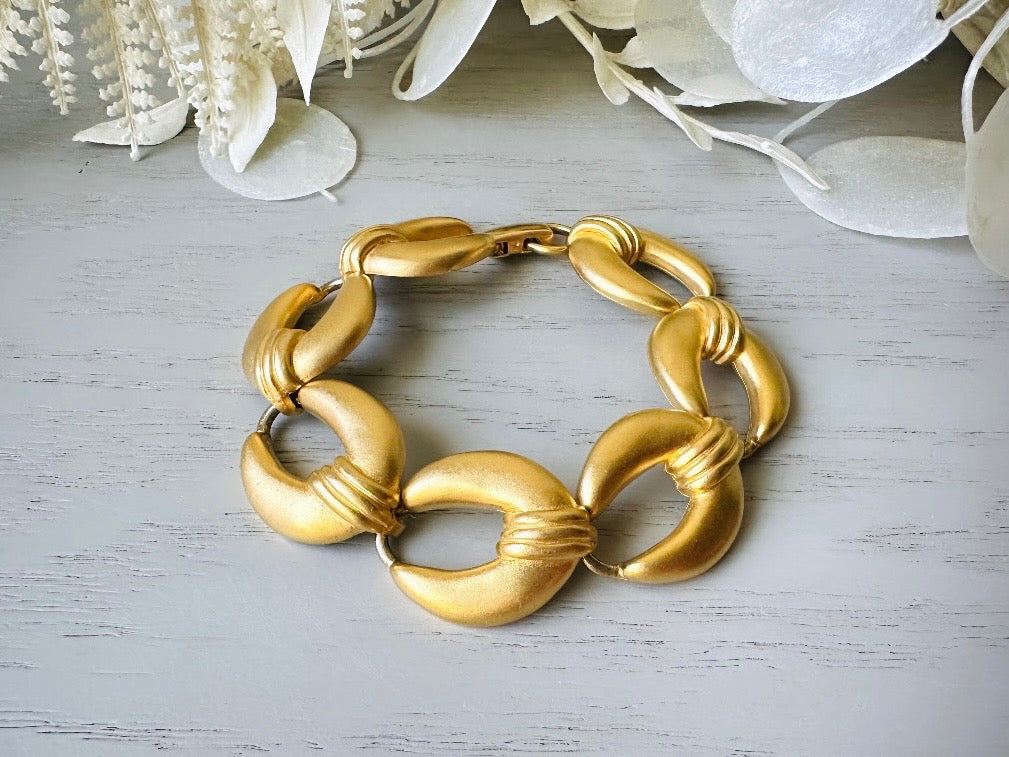 This is a matte gold chain link vintage bracelet by Premier Designs. The links are round and wide with textured ribbing in the center. The finish is a satin matte gold. Very popular style in the 1980s and modern.