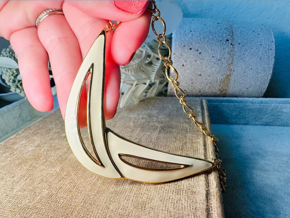 This cream and gold Monet vintage necklace is a striking classic. The focal pendant is an abstract asymmetrical crescent in gold with creamy enamel and sleek cut outs. This vintage designer necklace features gold cable chain and a signature Monet clasp and tag, also signed on back. This is a spectacular modernist jewelry piece to layer and easily goes with a variety of styles. Monet is renowned and well loved for beautiful jewelry that has stood the test of time. Excellent vintage condition, no flaws to not