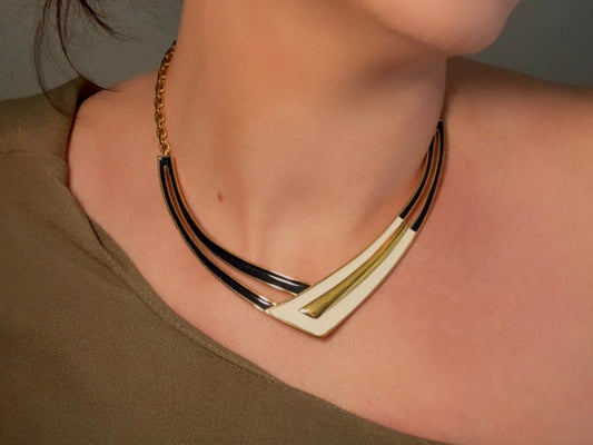 A close-up image of a vintage Monet necklace with a navy cream and gold enamel crescent pendant, featuring a gold curb chain and a signature Monet clasp.