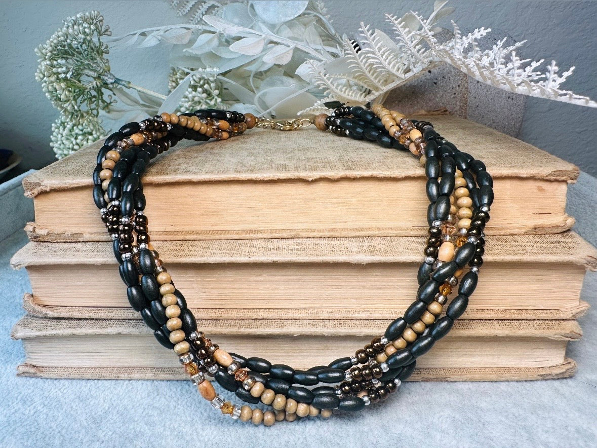 This vintage Napier necklace is a beautiful beaded twisted multistrand choker. Featuring six beaded strands in varying shapes and sizes composed of beads in wood, glass, acrylic, this bold necklace is a fabulous addition to your jewelry box. The beaded strands connect with a gold extension chain finished with a beautiful stamped Napier tag. Earthy black, brown and cream wood paired with gold, bronze and clear crystals- this necklace pairs beautifully with a variety of earrings and bracelets. Minimal wear in