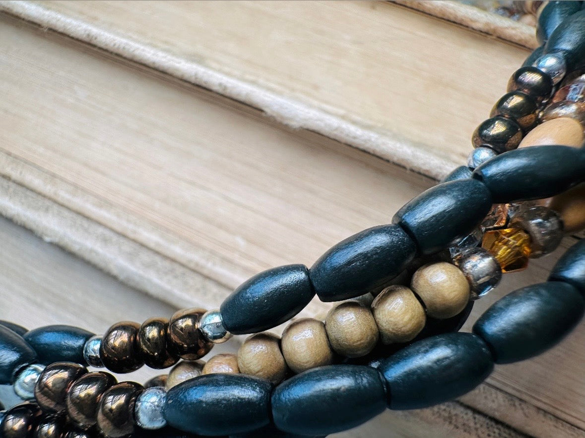 This vintage Napier necklace is a beautiful beaded twisted multistrand choker. Featuring six beaded strands in varying shapes and sizes composed of beads in wood, glass, acrylic, this bold necklace is a fabulous addition to your jewelry box. The beaded strands connect with a gold extension chain finished with a beautiful stamped Napier tag. Earthy black, brown and cream wood paired with gold, bronze and clear crystals- this necklace pairs beautifully with a variety of earrings and bracelets. Minimal wear in