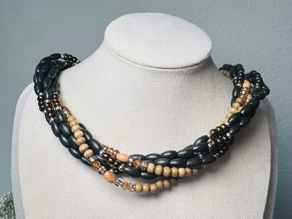 This vintage Napier necklace is a beautiful beaded twisted multistrand choker. Featuring six beaded strands in varying shapes and sizes composed of beads in wood, glass, acrylic, this bold necklace is a fabulous addition to your jewelry box. The beaded strands connect with a gold extension chain finished with a beautiful stamped Napier tag. Earthy black, brown and cream wood paired with gold, bronze and clear crystals- this necklace pairs beautifully with a variety of earrings and bracelets. Minimal wear in