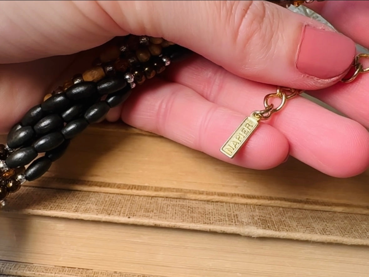 This vintage Napier necklace is a beautiful beaded twisted multistrand choker. Featuring six beaded strands in varying shapes and sizes composed of beads in wood, glass, acrylic, this bold necklace is a fabulous addition to your jewelry box. The beaded strands connect with a gold extension chain finished with a beautiful stamped Napier tag. 