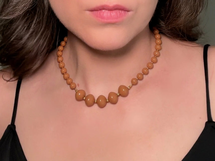 A vintage Park Lane designer necklace. The necklace is composed of 6mm caramel round beads with 5 bigger rondelle beads in the center with tiny gold spacer beads between. The necklace is worn on a model to show size reference.
