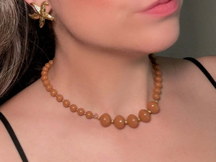 A vintage Park Lane designer necklace. The necklace is composed of 6mm caramel round beads with 5 bigger rondelle beads in the center with tiny gold spacer beads between. The necklace is worn on a model to show size reference.