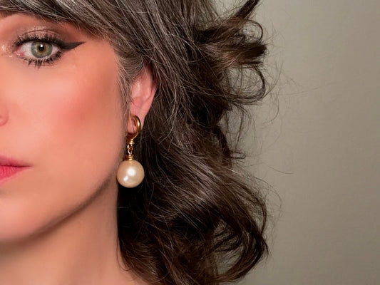 These vintage matte gold and cream pearl drop earrings are clip ons, shown on a model. They are very elegant. They give the appearance of half huggie hoops in a beautiful satin matte finish gold, with a striking oversized cream glass pearl. These Etruscan statement drop earrings are very on trend. These earrings are 2 inches long, unsigned in excellent condition.