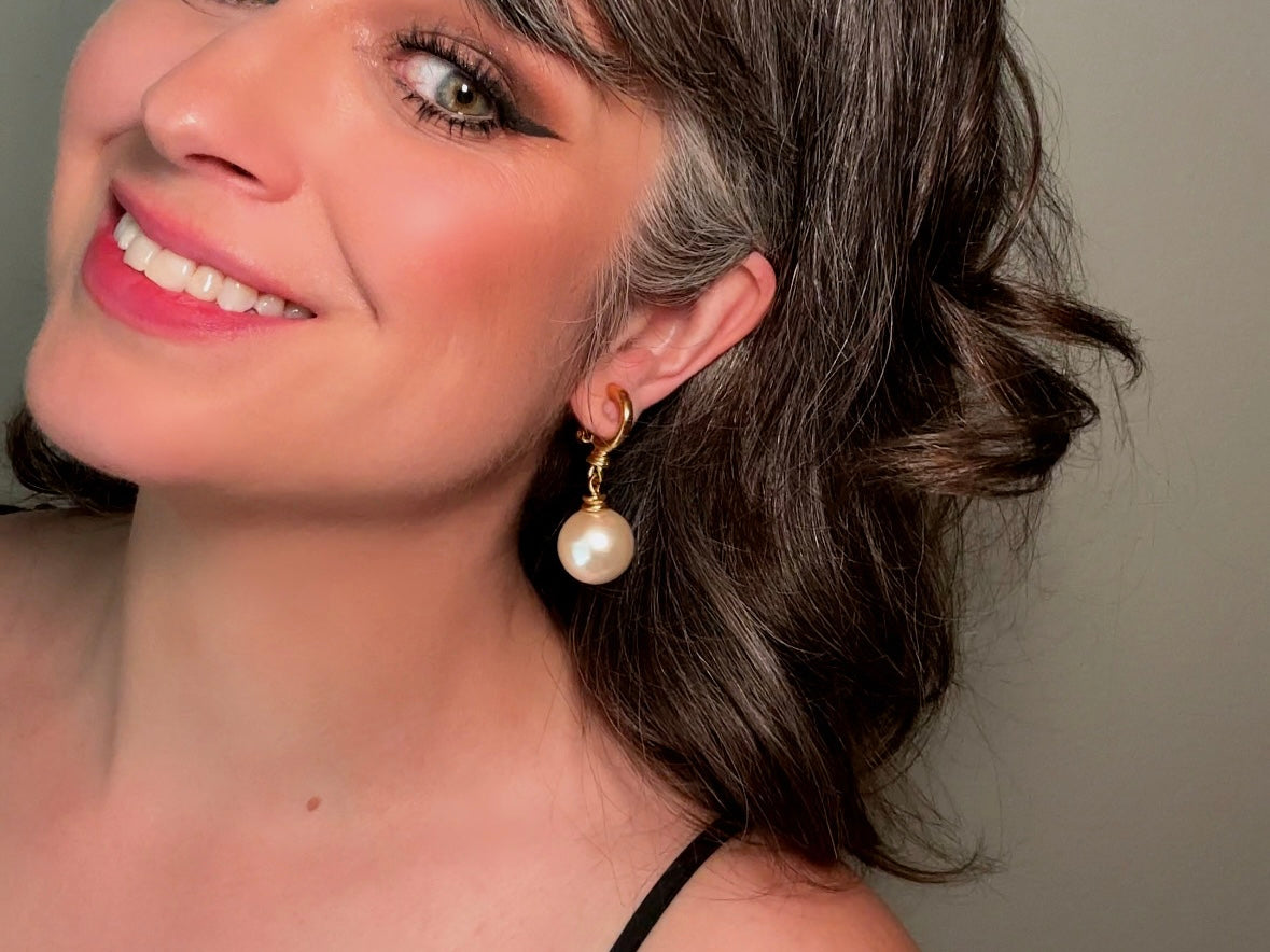 These vintage matte gold and cream pearl drop earrings are clip ons, shown on a model. They are very elegant. They give the appearance of half huggie hoops in a beautiful satin matte finish gold, with a striking oversized cream glass pearl. These Etruscan statement drop earrings are very on trend. These earrings are 2 inches long, unsigned in excellent condition.