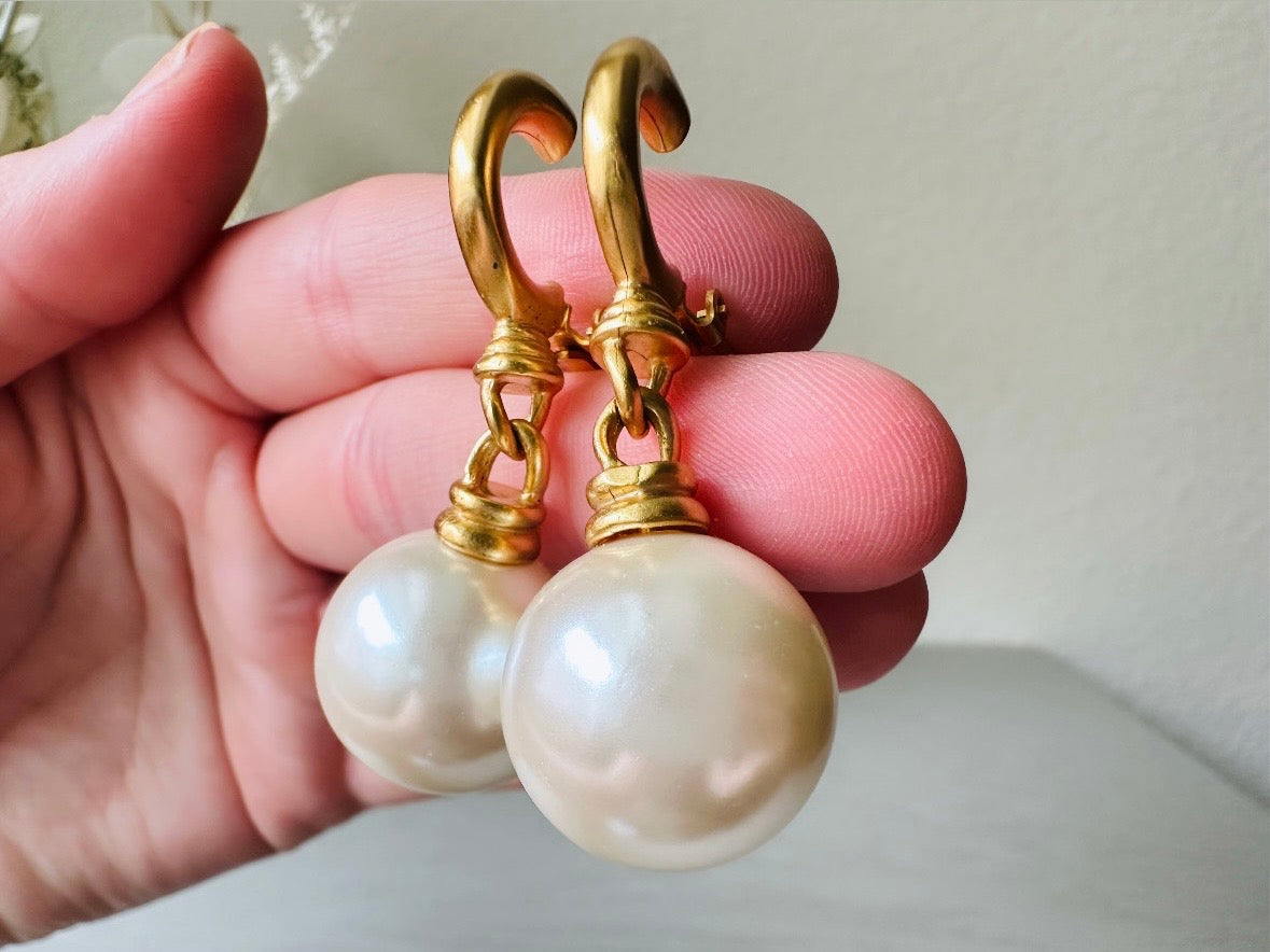 These vintage matte gold and cream pearl drop earrings are clip ons, shown on light gray background with white flowers. They are very elegant. They give the appearance of half huggie hoops in a beautiful satin matte finish gold, with a striking oversized cream glass pearl. These Etruscan statement drop earrings are very on trend. These earrings are 2 inches long, unsigned in excellent condition.