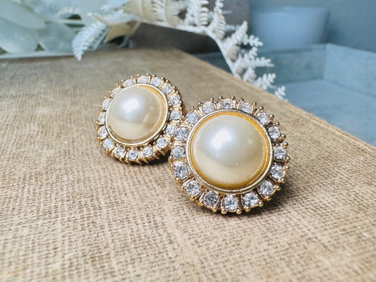 These gold and cream pearl button earrings are a classic old money aesthetic pair from the 80s. Featuring a beautiful cream faux pearl cabochon surrounded by a prong set rhinestone border. These clip on earrings are both unique and a timeless classic, old Hollywood glam style in great vintage condition. 

Dimensions: about 1", please view all pics for a visual size reference.
