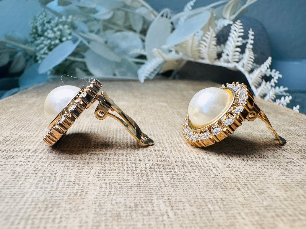 These gold and cream pearl button earrings are a classic old money aesthetic pair from the 80s. Featuring a beautiful cream faux pearl cabochon surrounded by a prong set rhinestone border. These clip on earrings are both unique and a timeless classic, old Hollywood glam style in great vintage condition. 

Dimensions: about 1", please view all pics for a visual size reference.
