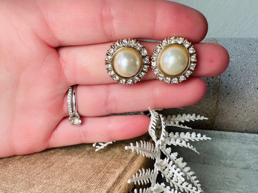 These gold and cream pearl button earrings are a classic old money aesthetic pair from the 80s. Featuring a beautiful cream faux pearl cabochon surrounded by a prong set rhinestone border. These clip on earrings are both unique and a timeless classic, old Hollywood glam style in great vintage condition. 

Dimensions: about 1", please view all pics for a visual size reference.
