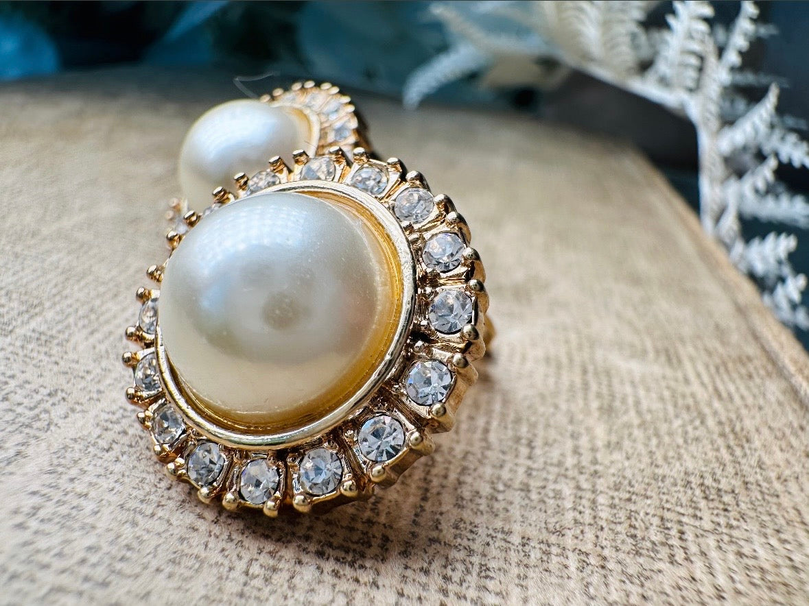 These gold and cream pearl button earrings are a classic old money aesthetic pair from the 80s. Featuring a beautiful cream faux pearl cabochon surrounded by a prong set rhinestone border. These clip on earrings are both unique and a timeless classic, old Hollywood glam style in great vintage condition. 

Dimensions: about 1", please view all pics for a visual size reference.
