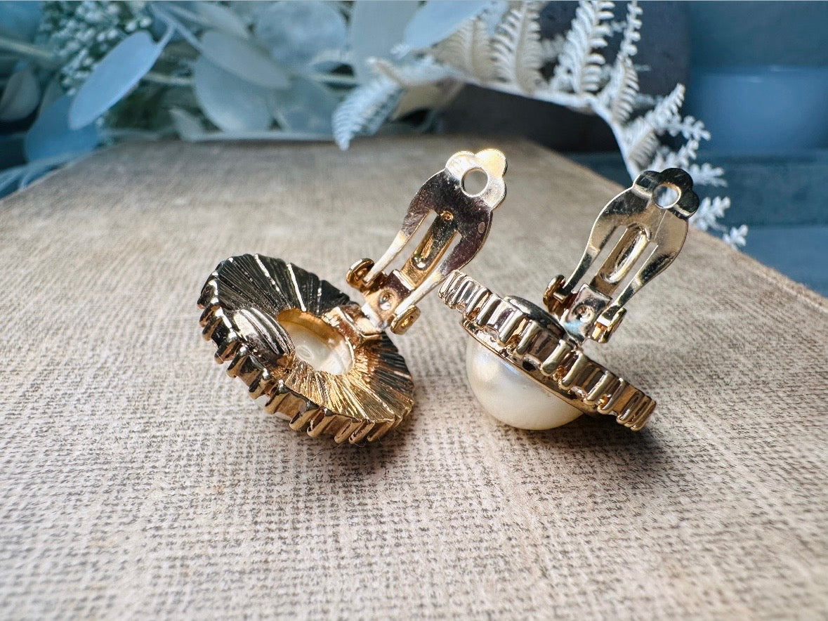 These gold and cream pearl button earrings are a classic old money aesthetic pair from the 80s. Featuring a beautiful cream faux pearl cabochon surrounded by a prong set rhinestone border. These clip on earrings are both unique and a timeless classic, old Hollywood glam style in great vintage condition. 

Dimensions: about 1", please view all pics for a visual size reference.
