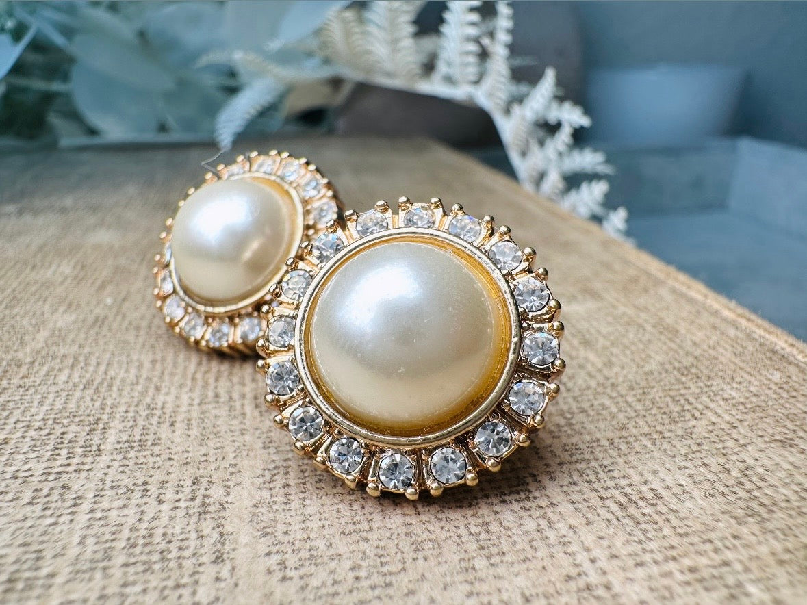 These gold and cream pearl button earrings are a classic old money aesthetic pair from the 80s. Featuring a beautiful cream faux pearl cabochon surrounded by a prong set rhinestone border. These clip on earrings are both unique and a timeless classic, old Hollywood glam style in great vintage condition. 

Dimensions: about 1", please view all pics for a visual size reference.
