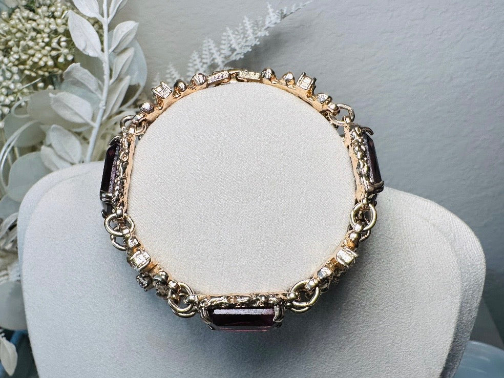 This 1970s faux amethyst vintage statement bracelet is gorgeous. Featuring three large smoky purple amethyst emerald cut stones prong set in gold. The setting is absolutely gorgeous in it's molten details- with a framed backing so the light can reflect through. Between each stone are golden branches in a brutalist style with small crystal accents. Absolutely beautiful vintage piece. Marked Sarah Coventry from 1973 Twilight collection. 