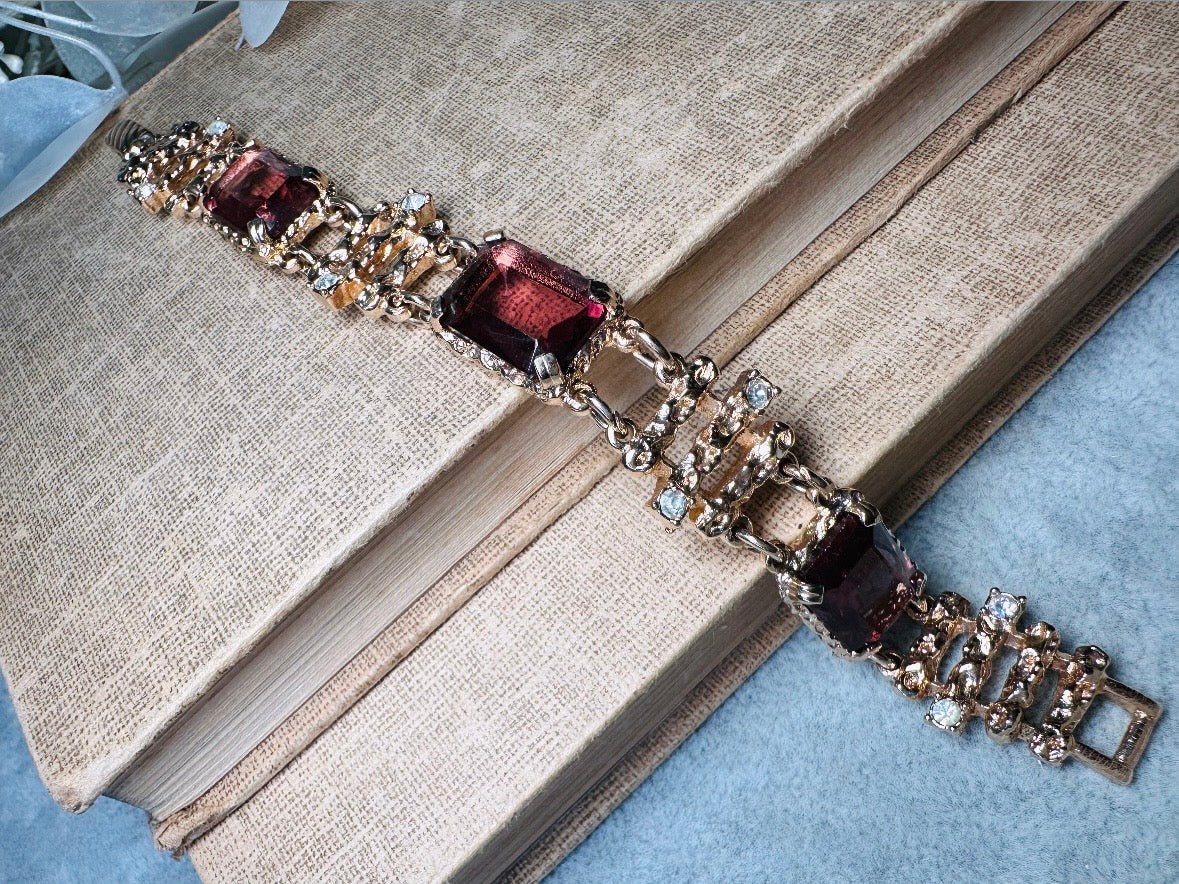 This 1970s faux amethyst vintage statement bracelet is gorgeous. Featuring three large smoky purple amethyst emerald cut stones prong set in gold. The setting is absolutely gorgeous in it's molten details- with a framed backing so the light can reflect through. Between each stone are golden branches in a brutalist style with small crystal accents. Absolutely beautiful vintage piece. Marked Sarah Coventry from 1973 Twilight collection. 