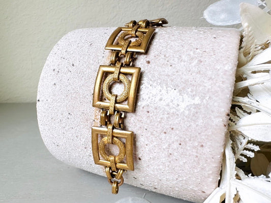 This is a vintage square link bracelet composed of antique gold geometric links. Featuring five structured squares with a floral embossed circle ring inside each one. This bold 1970s vintage chain bracelet is so unique; the circle inside of square and contrast of the bold shape with the royal floral motif is so interesting. It is 7 inches long in great vintage condition.