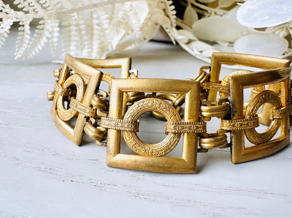 This is a vintage square link bracelet composed of antique gold geometric links. Featuring five structured squares with a floral embossed circle ring inside each one. This bold 1970s vintage chain bracelet is so unique; the circle inside of square and contrast of the bold shape with the royal floral motif is so interesting. It is 7 inches long in great vintage condition. Close up.