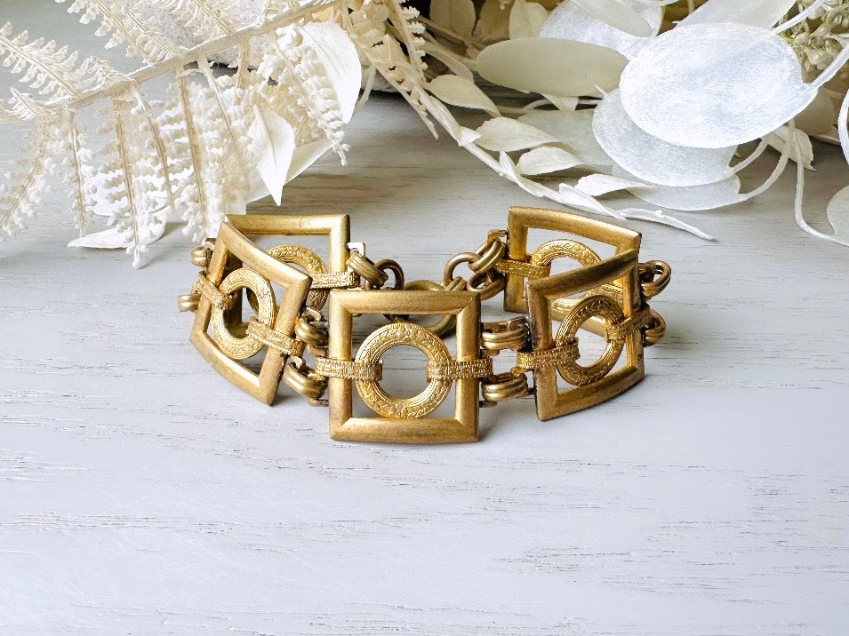 This is a vintage square link bracelet composed of antique gold geometric links. Featuring five structured squares with a floral embossed circle ring inside each one. This bold 1970s vintage chain bracelet is so unique; the circle inside of square and contrast of the bold shape with the royal floral motif is so interesting. It is 7 inches long in great vintage condition.