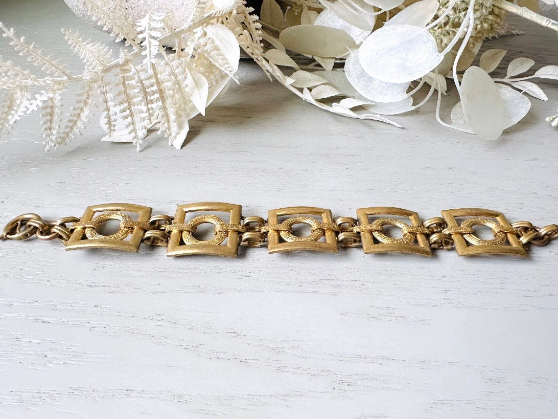 This is a vintage square link bracelet composed of antique gold geometric links. Featuring five structured squares with a floral embossed circle ring inside each one. This bold 1970s vintage chain bracelet is so unique; the circle inside of square and contrast of the bold shape with the royal floral motif is so interesting. It is 7 inches long in great vintage condition. Laid flat.