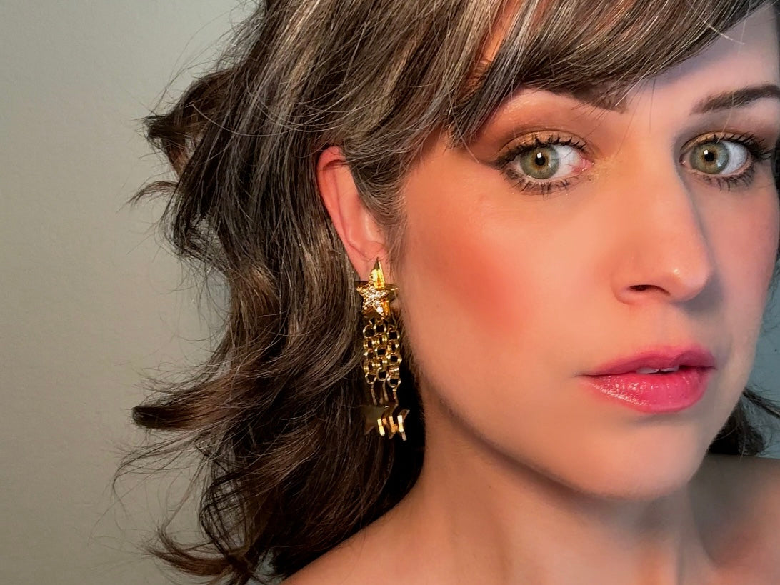 A pair of vintage gold star dangle earrings with a large gold star base with another layered star that is covered in pave set rhinestones. From this star three chain tassels drop, each with a gold star charm dangling from the end. These are clip on style, and in great condition. A fantastic 1980s pair!
