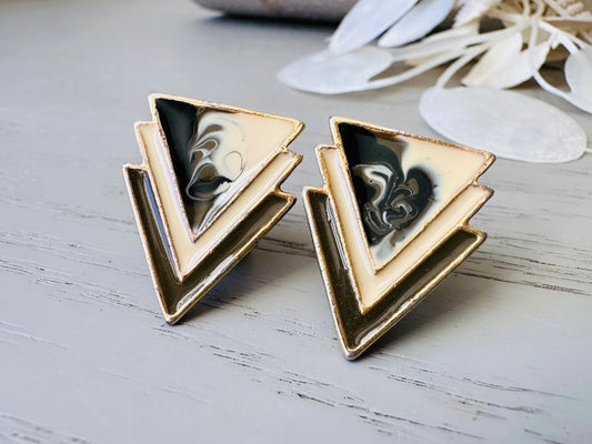 A pair of black, cream, and gold vintage triangle shaped earrings from the 1980s. The earrings are made of layered triangles with a marbled design.