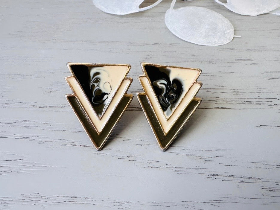 A pair of black, cream, and gold vintage triangle shaped earrings from the 1980s. The earrings are made of layered triangles with a marbled design.