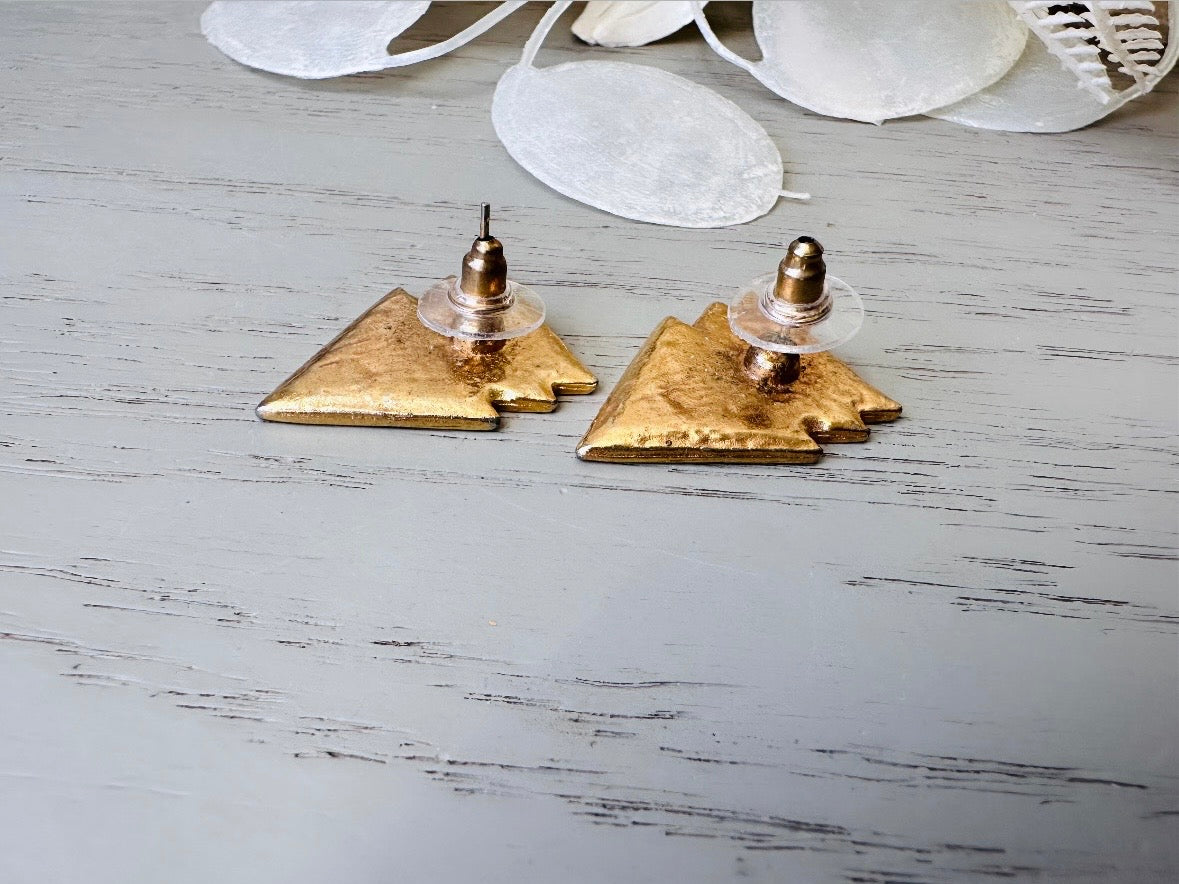 A pair of black, cream, and gold vintage triangle shaped earrings from the 1980s. The earrings are made of layered triangles with a marbled design. Pierced post backs