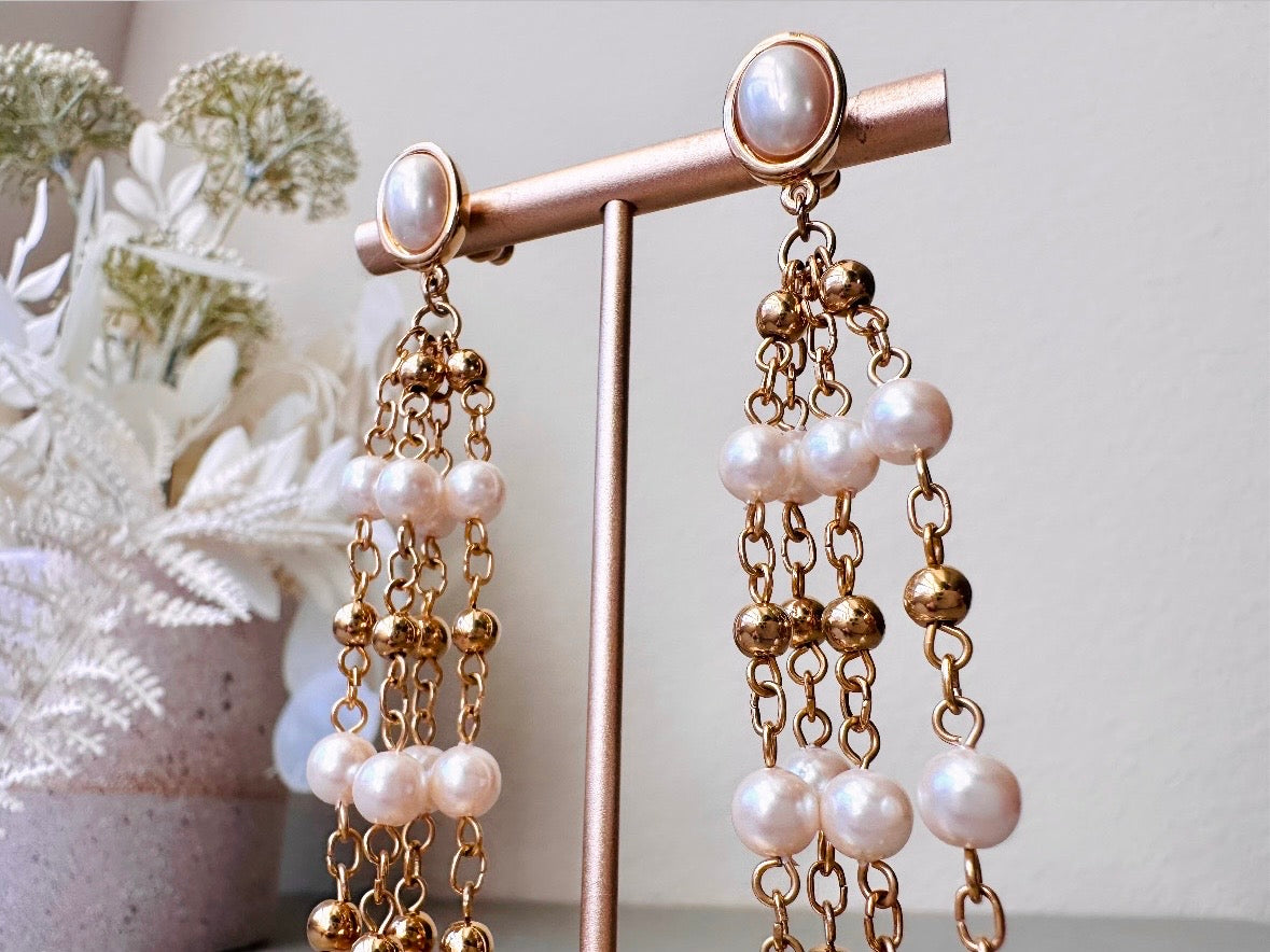 A pair of elegant vintage Trifari pearl chandelier earrings from the 1980s. These signed Trifari designer vintage earrings feature a cream pearl oval framed in gold as the post with a cascade of delicate long fine gold chain tassels with pearl links. In excellent vintage condition, they are three inches long. Close up to show details.