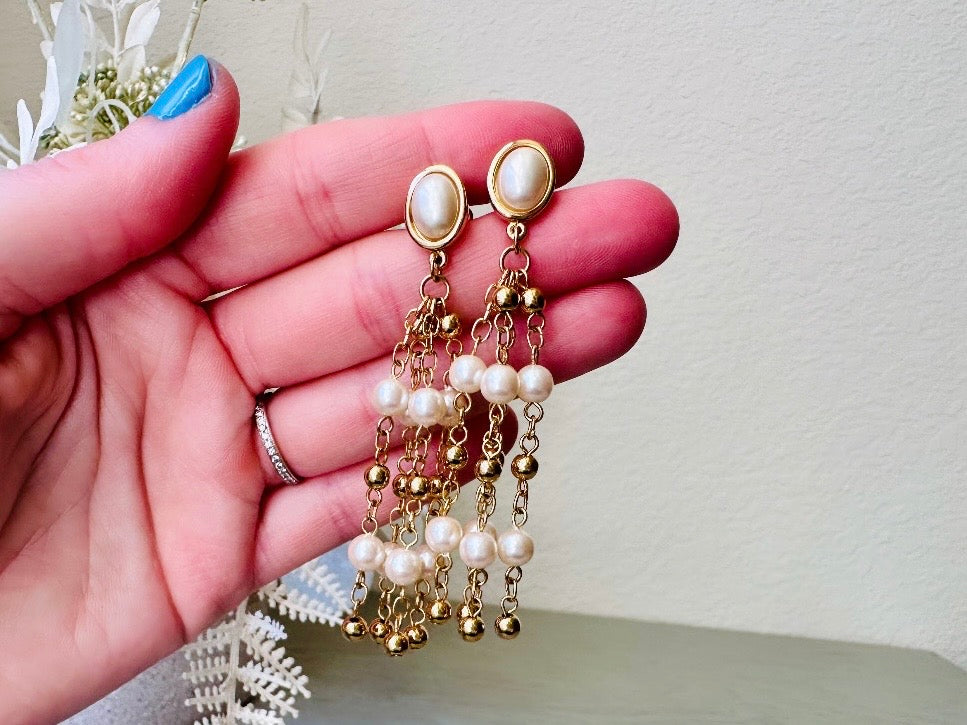 A pair of elegant vintage Trifari pearl chandelier earrings from the 1980s. These signed Trifari designer vintage earrings feature a cream pearl oval framed in gold as the post with a cascade of delicate long fine gold chain tassels with pearl links. In excellent vintage condition, they are three inches long. Held in hand for size reference.