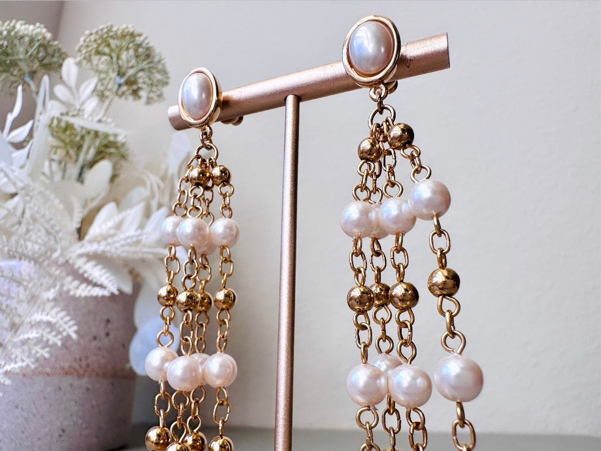 A pair of elegant vintage Trifari pearl chandelier earrings from the 1980s. These signed Trifari designer vintage earrings feature a cream pearl oval framed in gold as the post with a cascade of delicate long fine gold chain tassels with pearl links. In excellent vintage condition, they are three inches long. Close up shot.