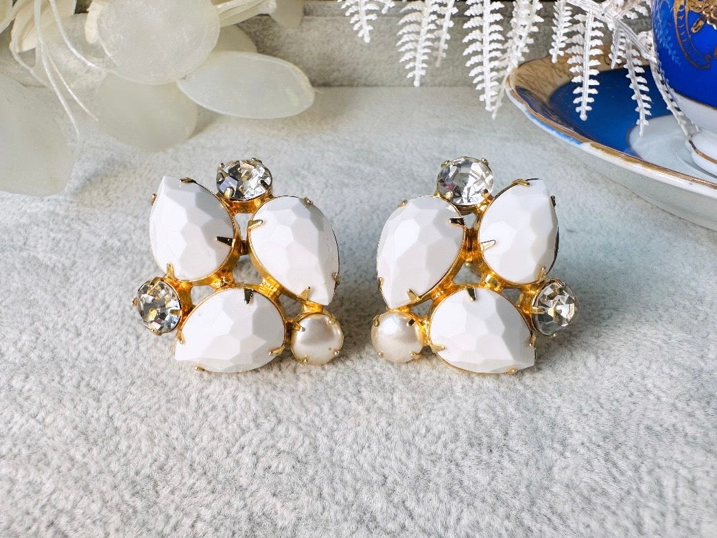 These vintage white earrings are an incredible pair of 1960s cluster earrings. Featuring opaque white faceted pear shaped stones, glass pearls and diamond rhinestones, these gold plated clip on earrings are fantastic. Each stone is prong set in a geometric pattern that mirrors each earring. A show-stopping rare pair of vintage earrings for a cocktail reception, award ceremony or wedding. Excellent vintage condition, please view all pics.