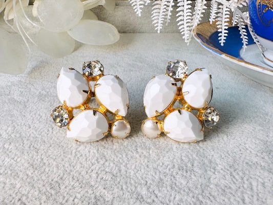 These vintage white earrings are an incredible pair of 1960s cluster earrings. Featuring opaque white faceted pear shaped stones, glass pearls and diamond rhinestones, these gold plated clip on earrings are fantastic. Each stone is prong set in a geometric pattern that mirrors each earring. A show-stopping rare pair of vintage earrings for a cocktail reception, award ceremony or wedding. Excellent vintage condition, please view all pics.